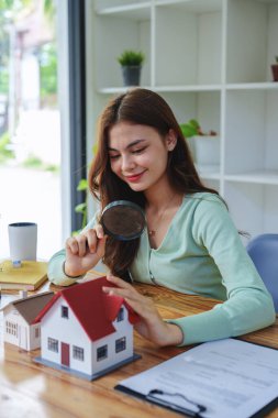 Müşteri bir ev modeli seçmek için bir büyüteç tutuyor, yatırım yapmaya karar vermeden önce konut kavramını gözden geçiriyor, kredi alıyor, sigorta yaptırıyor ve bankayla önemli belgeler imzalıyor.
