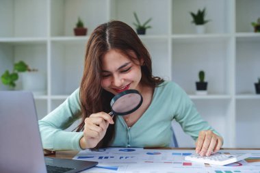 Melez bir kız, bir denetim çalışanı, elinde büyüteç olan bir muhasebeci ve vergi dairesinin yıllık vergi ödemelerini hesaplamak için hesap makinesi kullanan bir muhasebeci..
