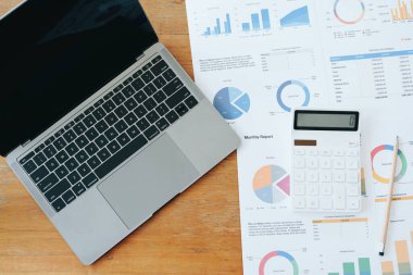 bilgisayar, hesap makinesi, bütçe ve finans belgeleri ve tahta masadaki kalem.