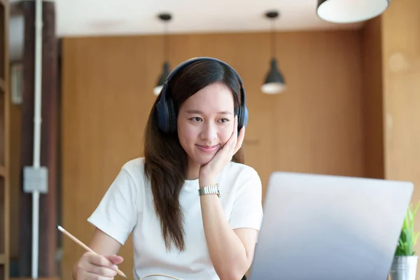 아시아의 컴퓨터를 사용하고 헤드폰을 노트북을 사용하여 도서관에 책상에서 비디오 회의를 — 스톡 사진