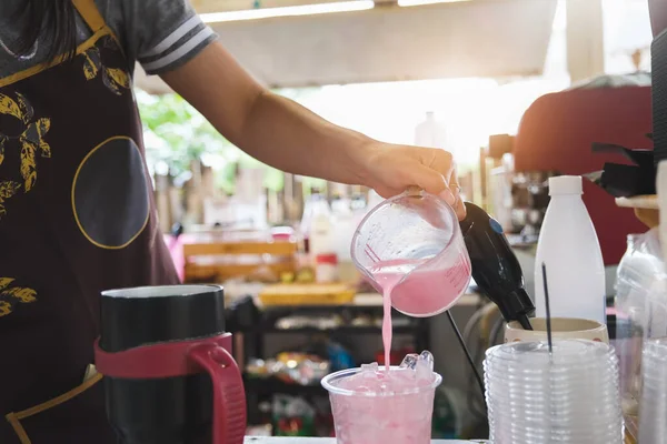 A female employee is pouring pink milk into a plastic cup for customers.