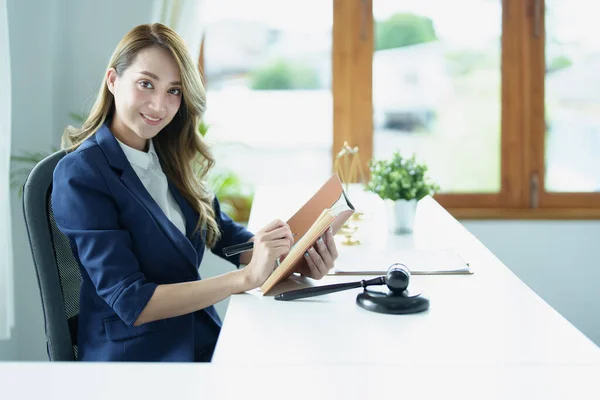 Portrait of a young Asian lawyer studying a lawsuit for a client using notebooks and paperwork on a desk.