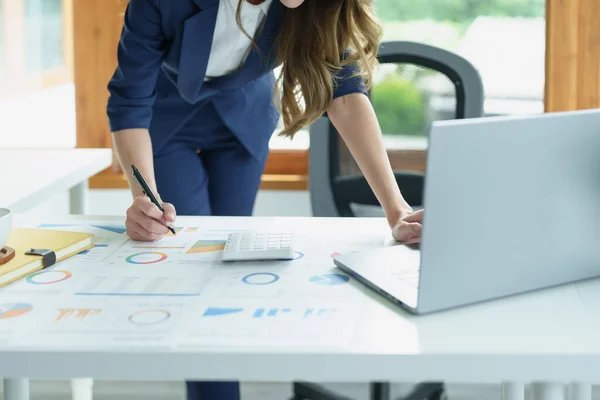 Düşünceli bir Asyalı iş kadınının portresi finansal tablolara bakıyor ve masasındaki bilgisayarı kullanarak pazarlama planları yapıyor..