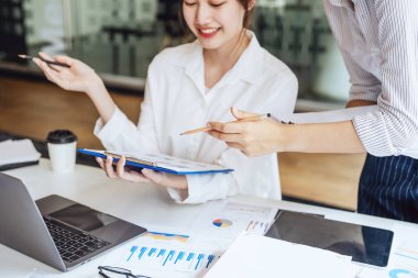 Müzakere, Analiz, Tartışma: Asyalı kadın ekonomist ve pazarlamacı, şirket için risk ve zararları önlemek için yatırım planlama amaçlı bir mali veri tablosuna işaret ediyor.