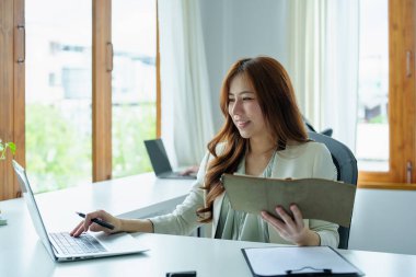 Finansal tabloları kapatmak için not defterleri, bütçe belgeleri ve bilgisayarlar kullanan Asyalı bir banka çalışanının portresi.