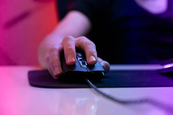 Gamer hand on mouse, close up photo of gamer hand on mouse with selective focus. Cyber sport gamer play game and click the mouse. Online player in a dark room with warm lights.