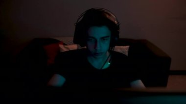 Genç oyuncu, genç oyuncu çevrimiçi video oyunu oynuyor. Odaklanmış oyuncu kişisel bilgisayarında oyun oynuyor. Odada renkli neon lambaları var. Kulaklık ve mikrofon takan genç bir çocuk.. 