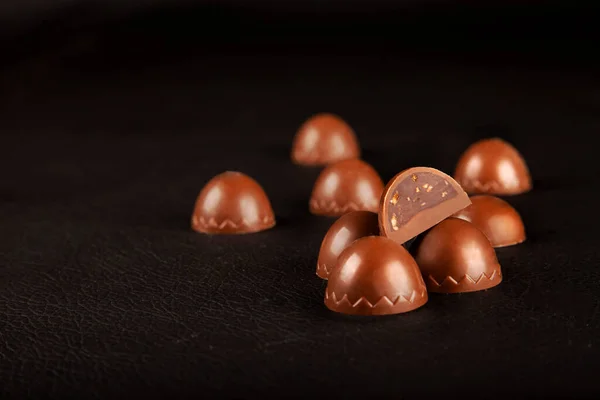 Chocolate candies, beautiful milky brown chocolate candies isolated on black background. Selective focus to one of the candies which cut half with copy space area.