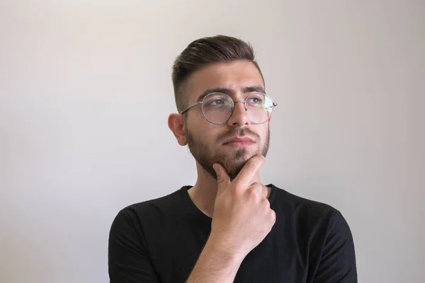 Teenager thinking, thoughtful caucasian brown haired teenager thinking and making decision. Portrait of young man in glasses looking up to copy space, touching his chin, isolated on grey background.