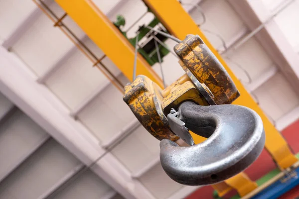 Crane hook, close up crane hook for overhead crane in factory. Bottom view or used and discolored yellow hook with factory concrete ceiling.