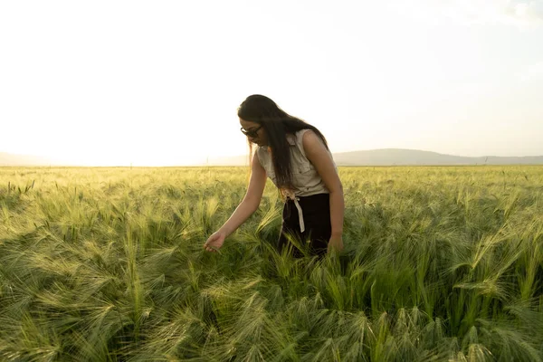 Female farmer, modern long haired female farmer. Casual dressed agronomist woman standing in the green wheat field. Controlling her crops by holding wheat ears. Agriculture businesswoman concept idea.