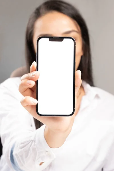 Holding smartphone, young woman holding smartphone in front of her face. Recommendation concept. New mobile phone with white blank screen for mockup in hand, showing close to camera vertical.