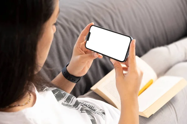 Smartphone mock up, caucasian woman have a break to reading book and holding smartphone mock up. Portrait of young lady watching movie or attending online meeting from her home with her cell phone.