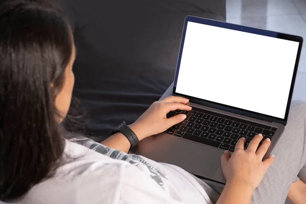 Modern laptop mock up,  over shoulder view of woman holding modern laptop mock up. Sitting on the couch, typing or watching or attending online meeting. Looking white blank screen of notebook computer