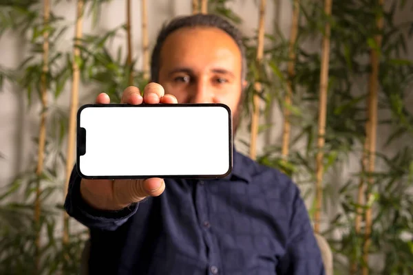 Holding smartphone, caucasian man holding smartphone horizontal. White blank screen for mock up. Modern male showing cell phone  display. Application recommendation, showing photo, movie concept idea.