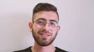 Looking at camera, closeup smiling young man looking at camera. Portrait of stubble beard teenage boys facial expressions. Sincerely smiling teen standing on isolated white background.