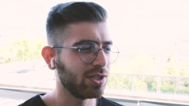 Telefonla konuşan, kendine güvenen genç iş adamı telefonla konuşuyor. Kablosuz kulaklık takarak coşkuyla konuşuyor. Müşterilere sorunları açıklamak, çalışanlara ne yapması gerektiğini söylemek. Yüz ifadeleri.