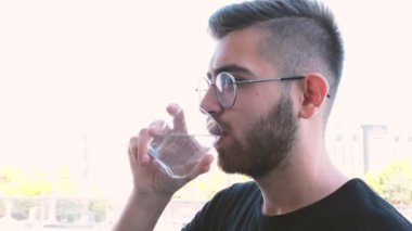 Su içen adam, yan görünüm yakın portre ya da su içen adam. Yakışıklı genç adam, susamış ve bir bardak saf su içiyor. Sağlıklı yaşam konsepti.