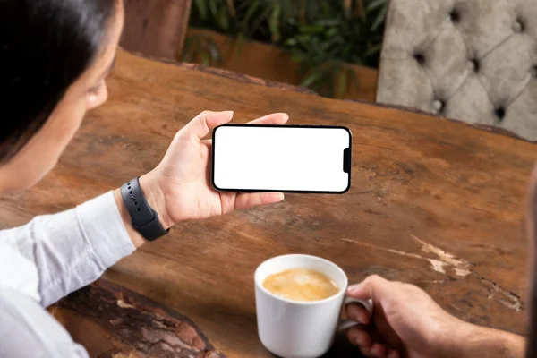 Showing smartphone horizontal, caucasian beautiful woman showing smartphone horizontal. Couple sitting  on wooden table drinking coffee and attending conference video call. Communication concept idea.