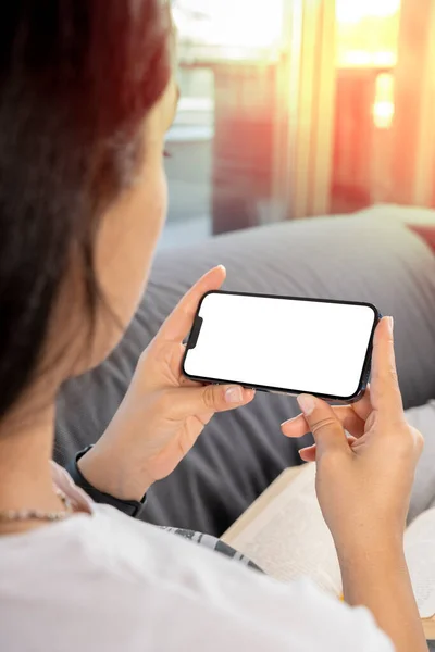 Horizontal phone mock up, young woman holding horizontal phone mock up. Over shoulder view of female watching from smartphone screen. Girl relaxing on the couch in morning photo with copy space.