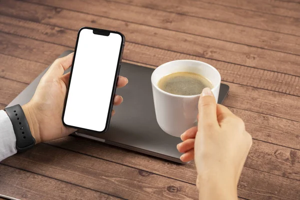 Video chat mock up, woman holding modern phone for video chat mock up. Application recommendation concept idea. Using laptop, drinking coffee and looking white blank screen of smartphone while sitting