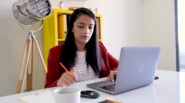 Laptop kullanan bir kadın, dizüstü bilgisayar kullanan bir ofis çalışanı portresi. Masada oturup, notlar almak ve çok çalışmak. Genç, güzel, esmer, iş yerinde beyaz bir model. Ofiste yoğun bir gün..