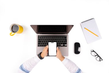 Dizüstü bilgisayarda çalışan bir kadın, dizüstü bilgisayarla çalışan bir kadının en iyi görüntüsü. Model yapmak için akıllı telefonu kullanıyor. Beyaz boş ekran. İş masası kurulumu, fare, defter, bardak, kahve içme. Beyazda izole edilmiş.