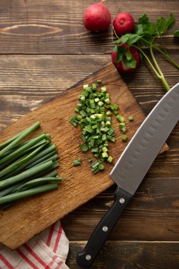 Yeşil soğan doğrama işlemi. Salata malzemeleri. Kırmızı turp mutfak havlusu ve maydanozla masanın üstünde yatıyor.