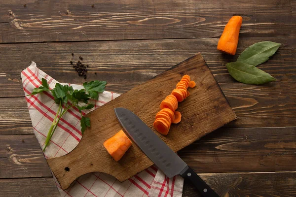 The process of cutting orange carrots into circles on a cutting board on a dark wooden background with a kitchen towel. Soup Ingredients. Soup Preparation.