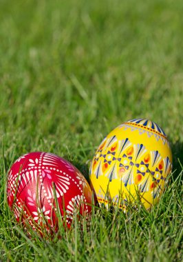 Two hand-painted Easter eggs lie in the grass in portrait format