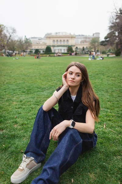 thoughtful young woman in sleeveless jacket sitting on lawn
