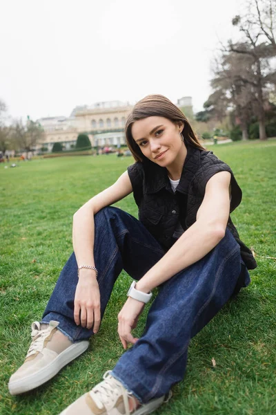 pretty young woman in sleeveless jacket sitting on lawn