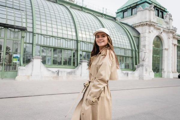 Cheerful Young Woman Trench Coat Baseball Cap Standing Hands Pockets — ストック写真