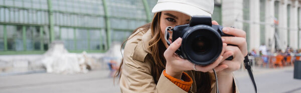 молодой фотограф в плаще и бейсболке, фотографирующий на цифровую камеру, баннер