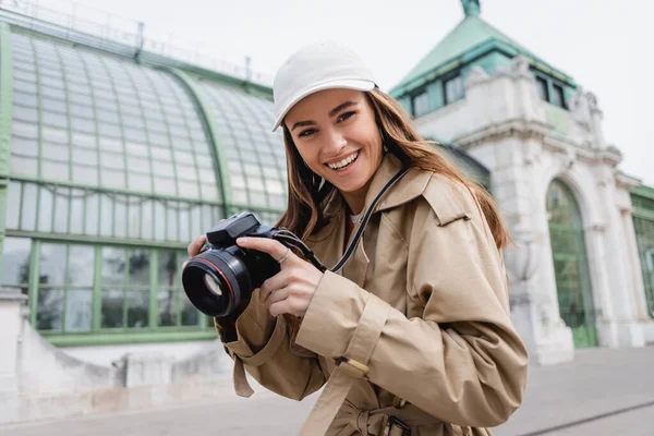 Mujer Alegre Gabardina Gorra Béisbol Sosteniendo Cámara Digital Ciudad Europea — Foto de Stock