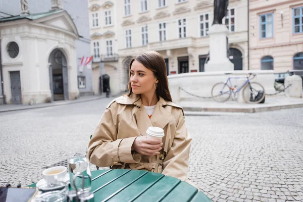 Young Woman Trendy Trench Coat Holding Coffee Cafe Terrace — ストック写真
