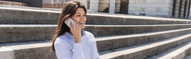 Şehirdeki beton merdivenlerde otururken akıllı telefondan konuşan mutlu bir kadın.