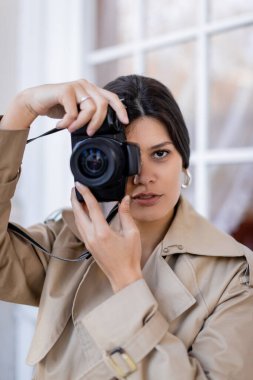 Trençkotlu esmer fotoğrafçı dijital kamerada fotoğraf çekiyor. 