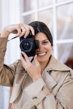 Trençkotlu mutlu fotoğrafçı dijital kamerada fotoğraf çekiyor. 