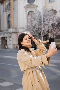 Şık ceketli neşeli kadın Viyana 'da akıllı telefondan selfie çekiyor.