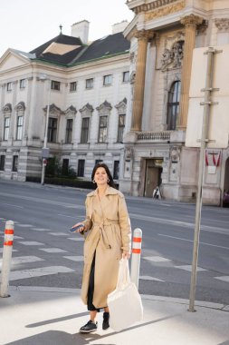 Viyana 'da şık montlu neşeli bir kadın çantalı ve akıllı telefonlu.
