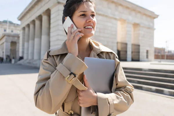 Vrolijke Vrouw Trench Jas Met Laptop Praten Smartphone Buiten — Stockfoto