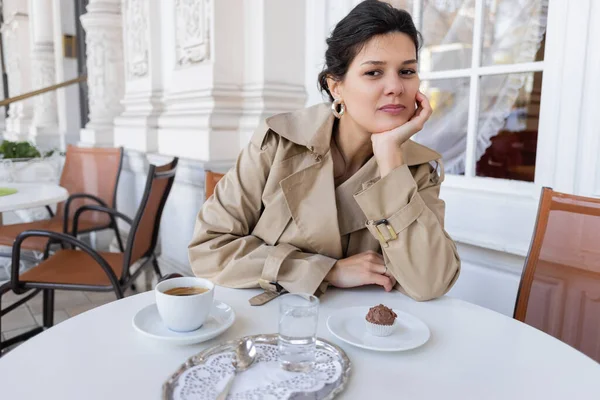 Μελαχρινή Γυναίκα Καμπαρντίνα Κάθεται Κοντά Cupcake Και Καφέ Στη Βεράντα — Φωτογραφία Αρχείου