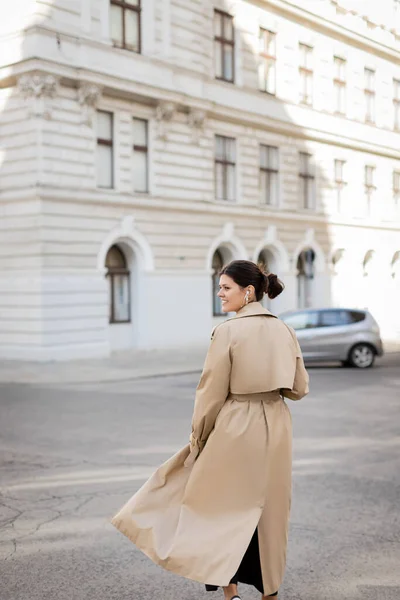ウィーンの路上を歩く有線イヤフォンやトレンチコートを着た幸せな女性 — ストック写真