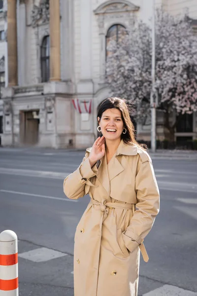 happy woman in elegant coat smiling on street in vienna