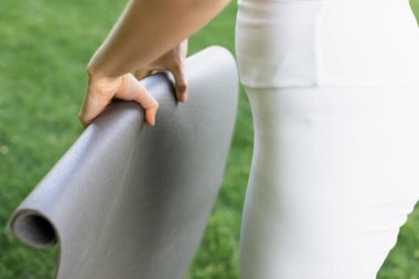 partial view of sportswoman holding fitness mat outdoors