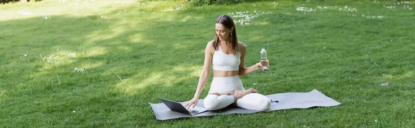 Beyaz spor giysili kadın, Lotus pozu verirken dizüstü bilgisayar kullanıyor.