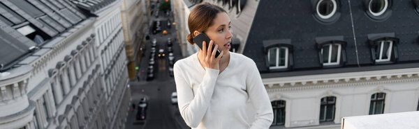 woman in white pullover talking on cellphone and looking away on rooftop, banner
