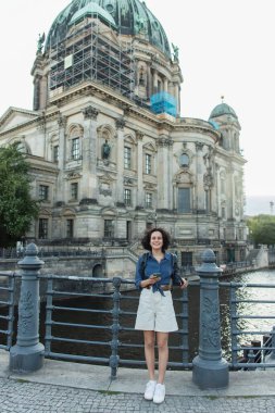BERLIN, GERMANY - JULY 14, 2020: happy young woman holding smartphone in front of berlin cathedral clipart