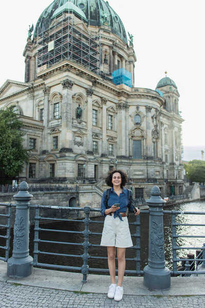 BERLIN, GERMANY - JULY 14, 2020: happy young woman holding smartphone in front of berlin cathedral